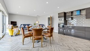 Un salon moderne comprenant un coin repas, une cuisine équipée d’appareils électroménagers en acier inoxydable et une grande fenêtre laissant entrer la lumière naturelle.