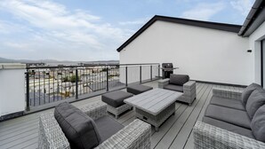 A rooftop terrace with wicker furniture, a barbecue, and a view of the cityscape. - Bayview Downings- Luxury 3 Bedroom First Floor Apt (Downings)
