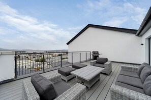 A rooftop terrace with wicker furniture, a barbecue, and a view of the cityscape. - Bayview Downings- Luxury 3 Bedroom First Floor Apt (Downings)