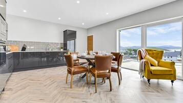 A modern kitchen with a dining area, large windows, and a yellow armchair.