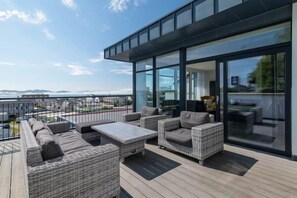 A modern outdoor deck with wicker furniture, a glass-enclosed area, and a view of the sea.