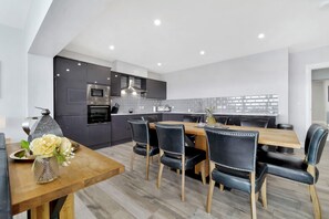 Une cuisine moderne avec des meubles de couleur sombre, une table à manger en bois et des chaises noires.