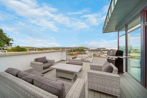 Une terrasse sur le toit, aménagée avec des meubles en osier, un barbecue et offrant une vue sur le paysage urbain.