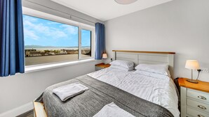 Et hotelværelse med et stort vindue, en seng med hvide sengetøj, et natbord med en lampe og udsigt til bybilledet.