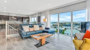 Ein geräumiger Wohnbereich mit einem modernen Sofa, einem Holztisch und Blick auf die Stadt durch große Fenster.