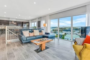 Een ruime woonkamer met een moderne bank, een houten salontafel en een uitzicht op de stad door grote ramen.