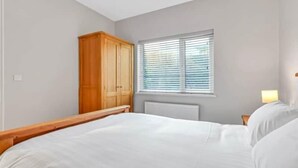 Ein Schlafzimmer mit einem Bett, einem Holzschrank, einem Fenster mit Jalousien und einem Nachttisch mit Lampe.
