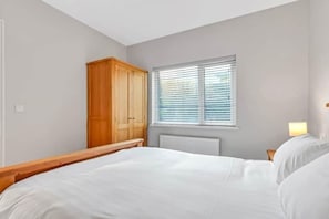 Een slaapkamer met een bed, een houten garderobe, een raam met zonwering en een nachtkastje met een lamp.