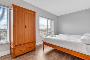 Une chambre à coucher avec un cadre de lit en bois, une grande armoire et deux fenêtres équipées de stores.