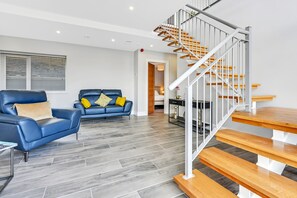 Un salon moderne avec un canapé en cuir bleu, un escalier en bois et un revêtement de sol en carrelage gris.