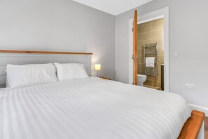 A neatly made bed with white linens, a wooden headboard, and a bedside lamp.