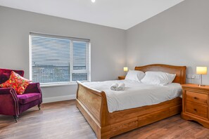 Une chambre à coucher avec un lit en bois, un fauteuil violet et une fenêtre avec des stores.
