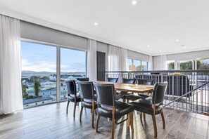A dining area with a large table and chairs, large windows with curtains, and a view of the cityscape.