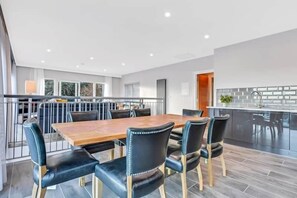 A modern dining area with a wooden table and black upholstered chairs, a kitchen with a glass backsplash, and a view of the outdoors.