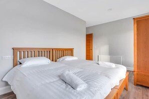 Una cama bien tendida con cabecera de madera en una habitación con paredes de colores claros y suelo de madera.