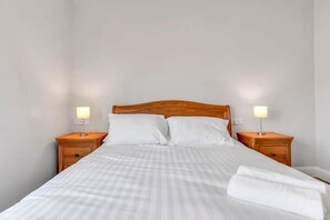 A single bed with a wooden headboard, two bedside tables with lamps, and a neatly made bed with white linens. - Bayview Downings - Luxury 4 Bedroom Villa (Downings)