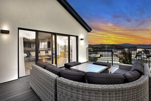 Un balcón moderno al aire libre con mobiliario de mimbre y una puerta de cristal que da a un espacio interior.