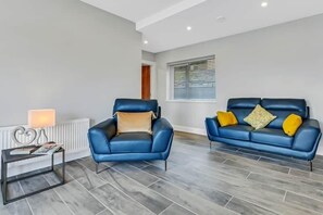Un salon moderne avec deux canapés en cuir bleu, une petite table d’appoint avec une lampe et un radiateur.