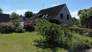 A house with a sloped roof, a visible chimney, and a well-maintained garden with various plants and flowers. - Quietly located vacation apartment near the dike (Wurster Nordseeküste)