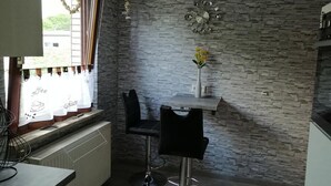 A kitchen with a stone wall, a window with curtains, a table with two chairs, and a vase with flowers. - Quietly located vacation apartment near the dike (Wurster Nordseeküste)