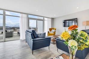 A modern living room with a large window, a sofa, a yellow armchair, a coffee table, and a vase with flowers.