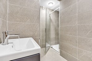 A bathroom with a white sink, a glass shower enclosure, and beige tiled walls.