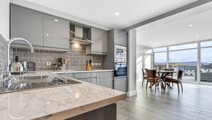 A modern kitchen with grey cabinets, a marble countertop, and a dining area with a view. - Bayview Downings - Luxury 2 Bedroom Apartment (Downings)