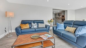 A modern living room with two blue leather sofas, a wooden coffee table, and a floor lamp. - Bayview Downings - Luxury 2 Bedroom Apartment (Downings)
