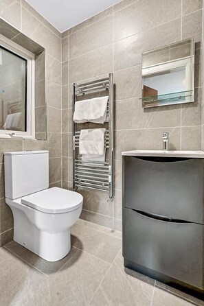 A modern bathroom with a toilet, a sink, a towel rack, and a mirror. - Bayview Downings - Luxury 2 Bedroom Apartment (Downings)