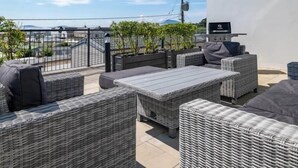 A rooftop patio with wicker furniture, a grill, and a view of the cityscape. - Bayview Downings - Luxury 2 Bedroom Apartment (Downings)
