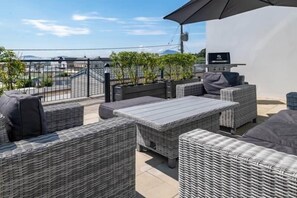 Una terraza en la azotea con mobiliario de mimbre, una parrilla y vistas a la ciudad.