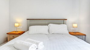 A neatly made bed with white linens and two pillows, flanked by wooden nightstands with lamps. - Bayview Downings - Luxury 2 Bedroom Apartment (Downings)