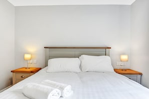 A neatly made bed with white linens and two pillows, flanked by wooden nightstands with lamps. - Bayview Downings - Luxury 2 Bedroom Apartment (Downings)