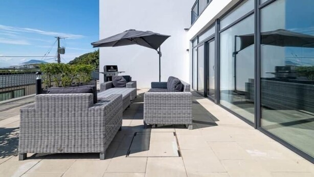 A rooftop patio with wicker furniture, a large umbrella, and a glass building in the background. - Bayview Downings - Luxury 2 Bedroom Apartment (Downings)