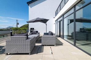 Una terraza en la azotea con muebles de mimbre, un paraguas grande y un edificio de cristal al fondo.