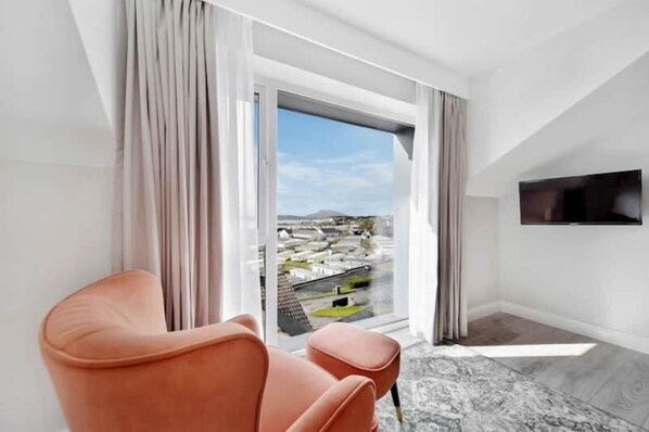 A modern room with a large window, a flat-screen TV mounted on the wall, and a single orange chair. - The View, Downings - Luxury House (Downings)