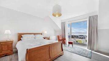 Un dormitorio moderno con una cama grande, una mesita de noche, una silla y vistas de la ciudad a través de un amplio ventanal.