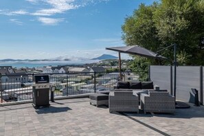 An outdoor patio with seating and a grill, overlooking a scenic view of a body of water and distant mountains. - The View, Downings - Luxury House (Downings)