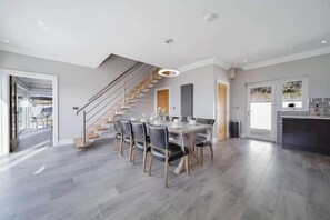 A spacious dining area with a modern staircase, a kitchen with a dark countertop, and a view of the outdoors. - The View, Downings - Luxury House (Downings)