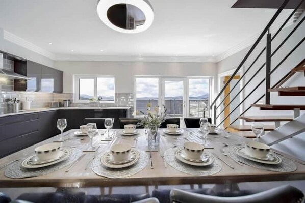 A modern dining area with a large table set for six, surrounded by large windows offering a view of the cityscape. - The View, Downings - Luxury House (Downings)