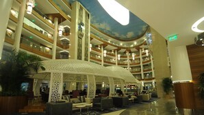 Un hall d’hôtel à plusieurs niveaux, doté d’un espace de réception central ouvert, de plusieurs étages et d’un plafond au design incurvé.