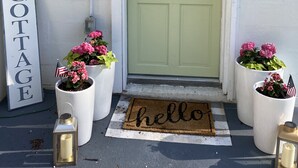 Eine grüne Tür mit einer weißen Fußmatte, auf der "hello" steht, ein Willkommen-Schild und zwei Ünterpötter mit amerikanischen Flaggen.