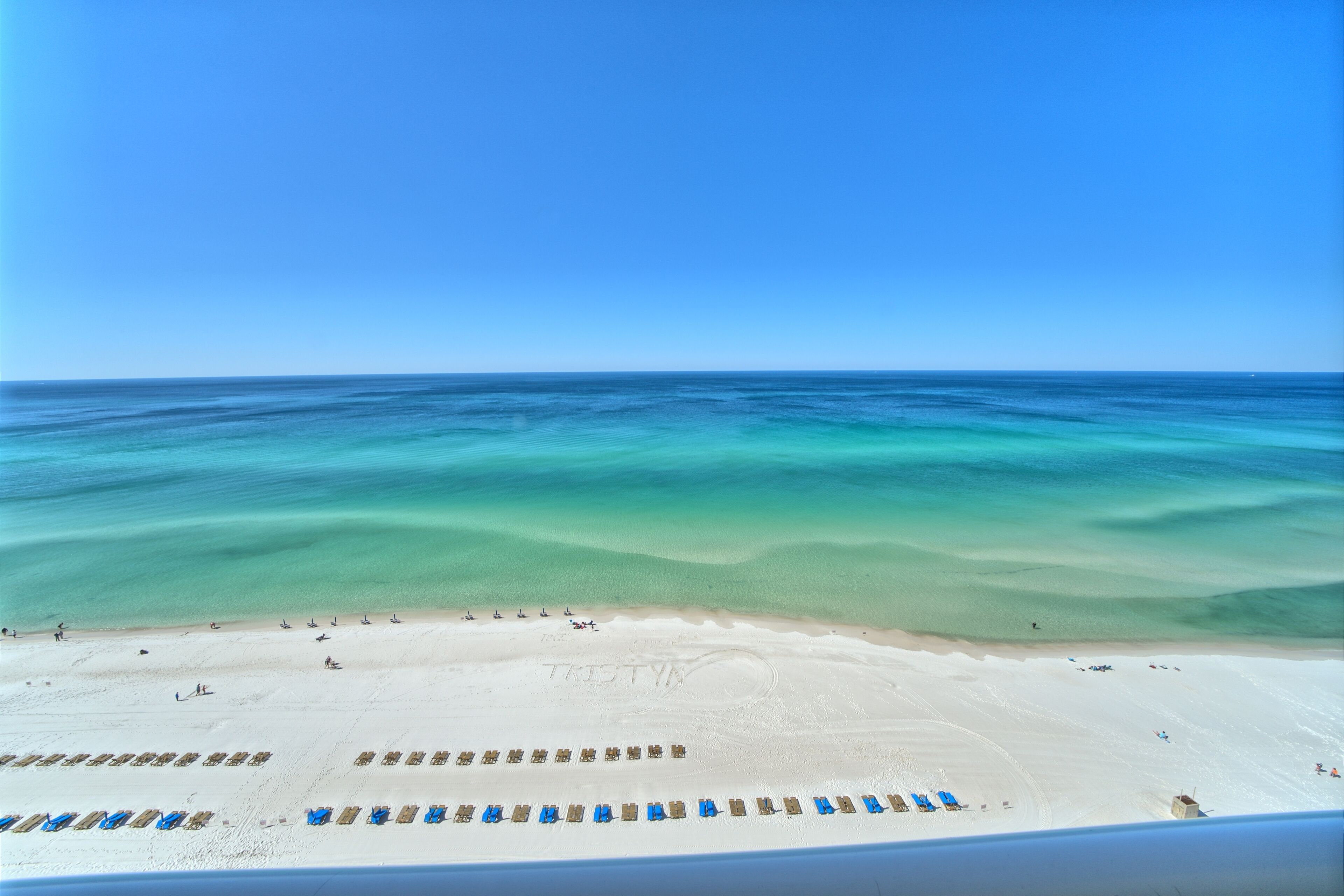 A beach with clear turquoise waters, a sandy shore, and rows of beach chairs.