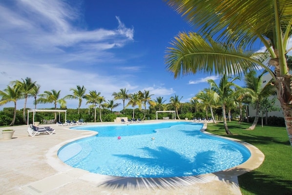 A large, curved swimming pool surrounded by palm trees and lounge chairs.