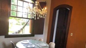Un comedor con una mesa redonda para cuatro personas, una araña y vistas al exterior a través de una ventana.