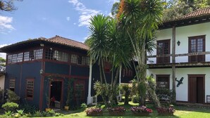 Un edificio de dos pisos con techo de tejas, un balcón y un jardín con palmeras y flores.