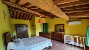 Un dormitorio con techo de madera, una cama con cubrecama blanco, un aparador, una cuna y una puerta verde.