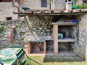 A rustic outdoor kitchen area with a brick oven, a table with a colorful tablecloth, and a green chair.