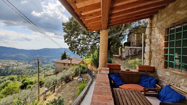Una terraza de madera con vistas a un paisaje rural, un muro de piedra y una casa tradicional al fondo.