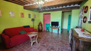 Una sala de estar con un sofá rojo, una mesita redonda pequeña, un televisor y un aparador de madera.